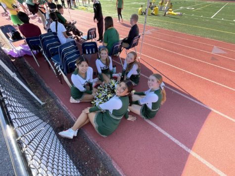 Five cheerleaders sit in a circle on the track.