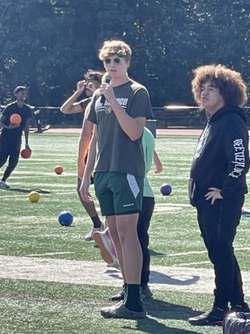 Student holding a microphone on the field with a second student standing next to him.
